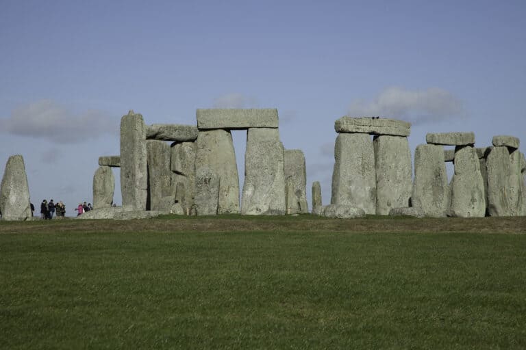Ancient stone circle with standing stones set in a field under a blue sky.