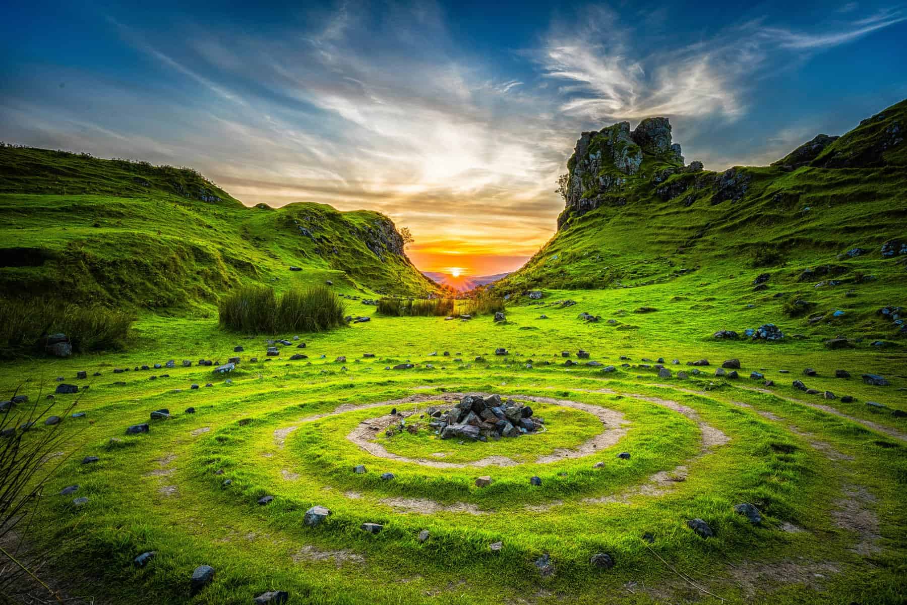 Peaceful landscape featuring lush grass, rocks, and a sunset sky.