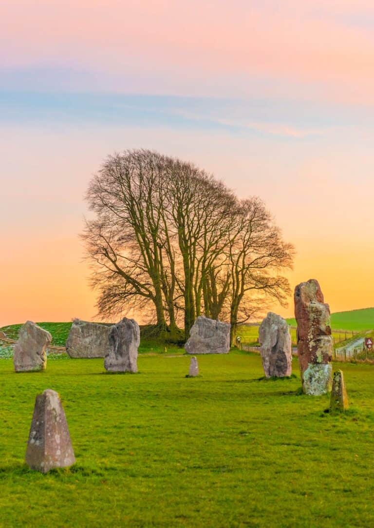 Old stone circle with moss-covered monoliths and a large tree during dusk.
