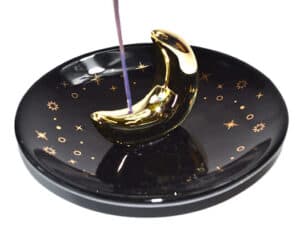 Incense holder shaped like a crescent moon with purple incense stick on a celestial-themed dish.