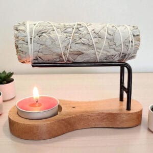 Modern wooden stand with sage bundle, candle, and small potted plants for spiritual practices.