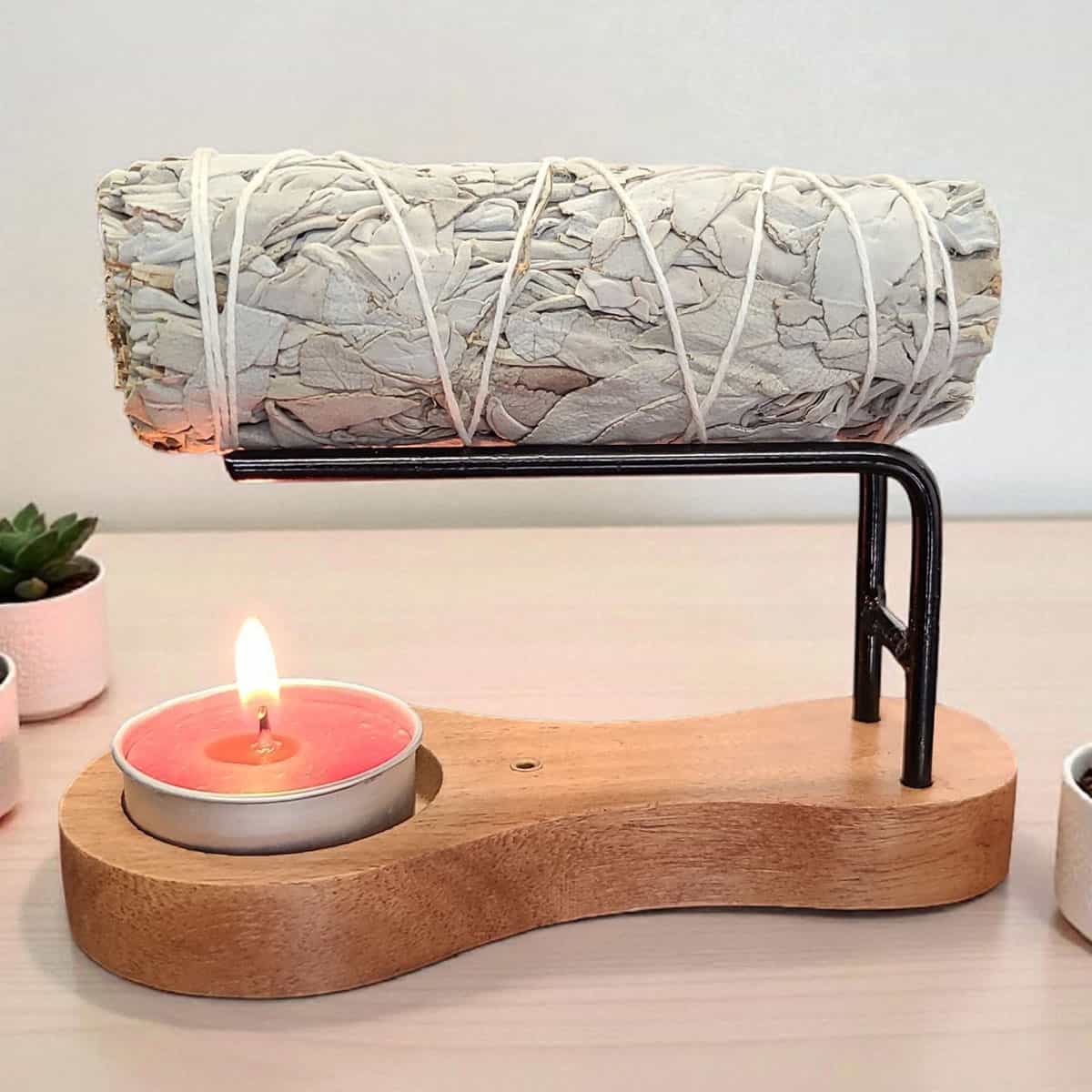 Modern wooden stand with sage bundle, candle, and small potted plants for spiritual practices.