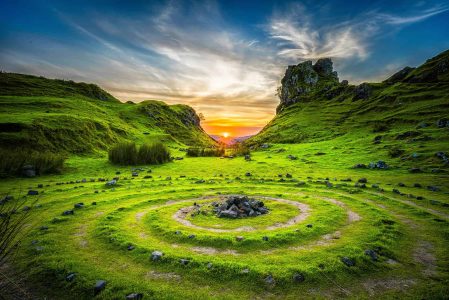 Peaceful landscape featuring lush grass, rocks, and a sunset sky.