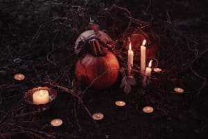 Alt: Pumpkin with lit candles and twigs on dark soil, surrounded by bare branches and leaves.
