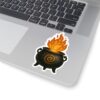 Decorative sticker of a black cauldron with a spiral symbol, spewing fiery flames, placed on a silver laptop keyboard.