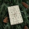 A gift wrapped in paper decorated with indigenous symbols and plant motifs, set among natural pine greenery and cones.