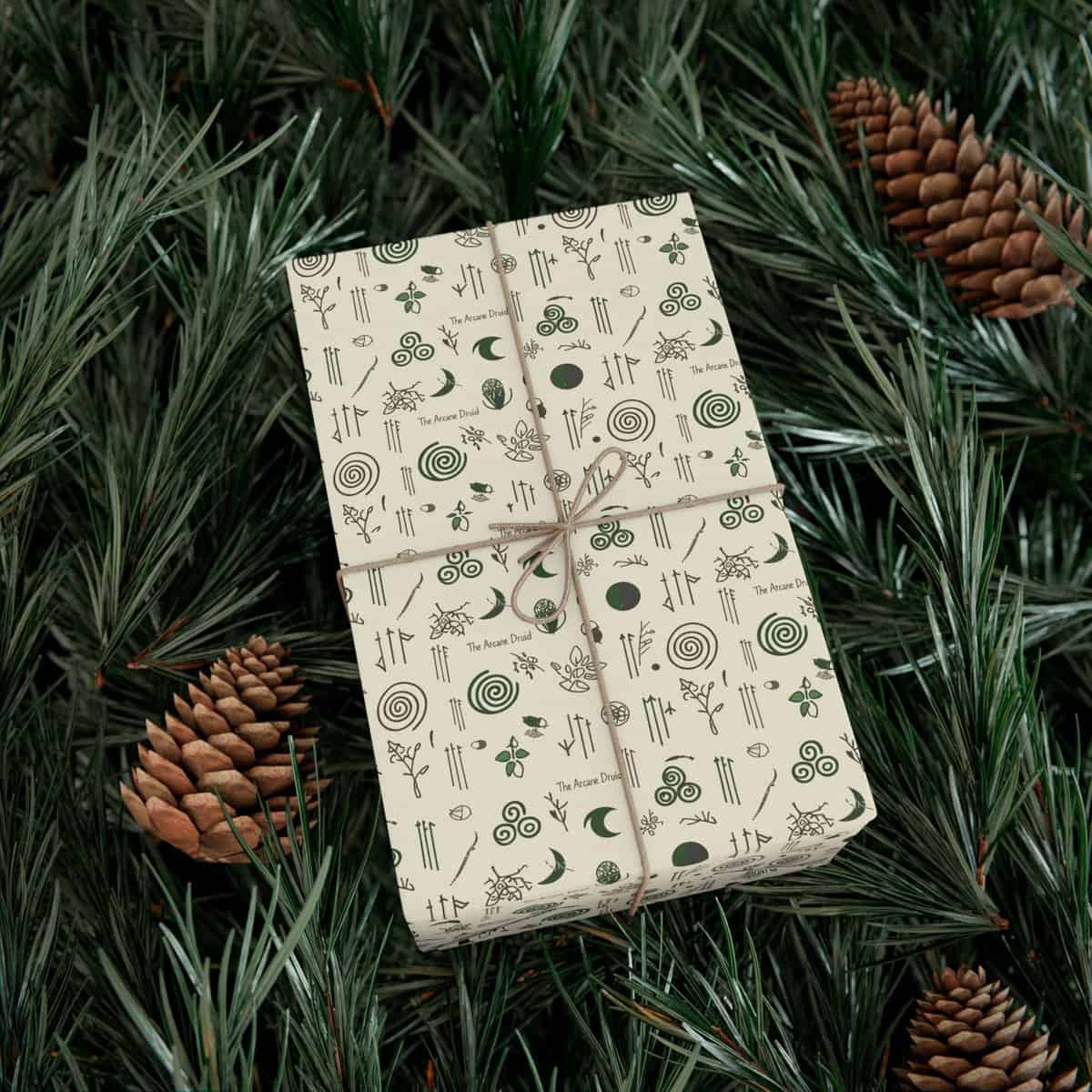 A gift wrapped in paper decorated with indigenous symbols and plant motifs, set among natural pine greenery and cones.