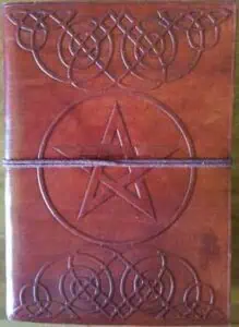 A wooden cover featuring intricate Celtic knotwork and a central pentagram symbol, bound with a leat.