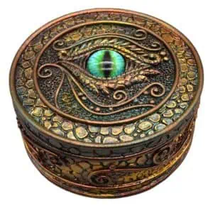 An ornate, round box with a detailed eye design on the lid, featuring a vibrant green iris and intri.