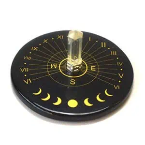 A round black disc with gold markings, moon phases, and cardinal directions, featuring a clear cryst.