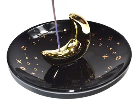 Incense holder shaped like a crescent moon with purple incense stick on a celestial-themed dish.
