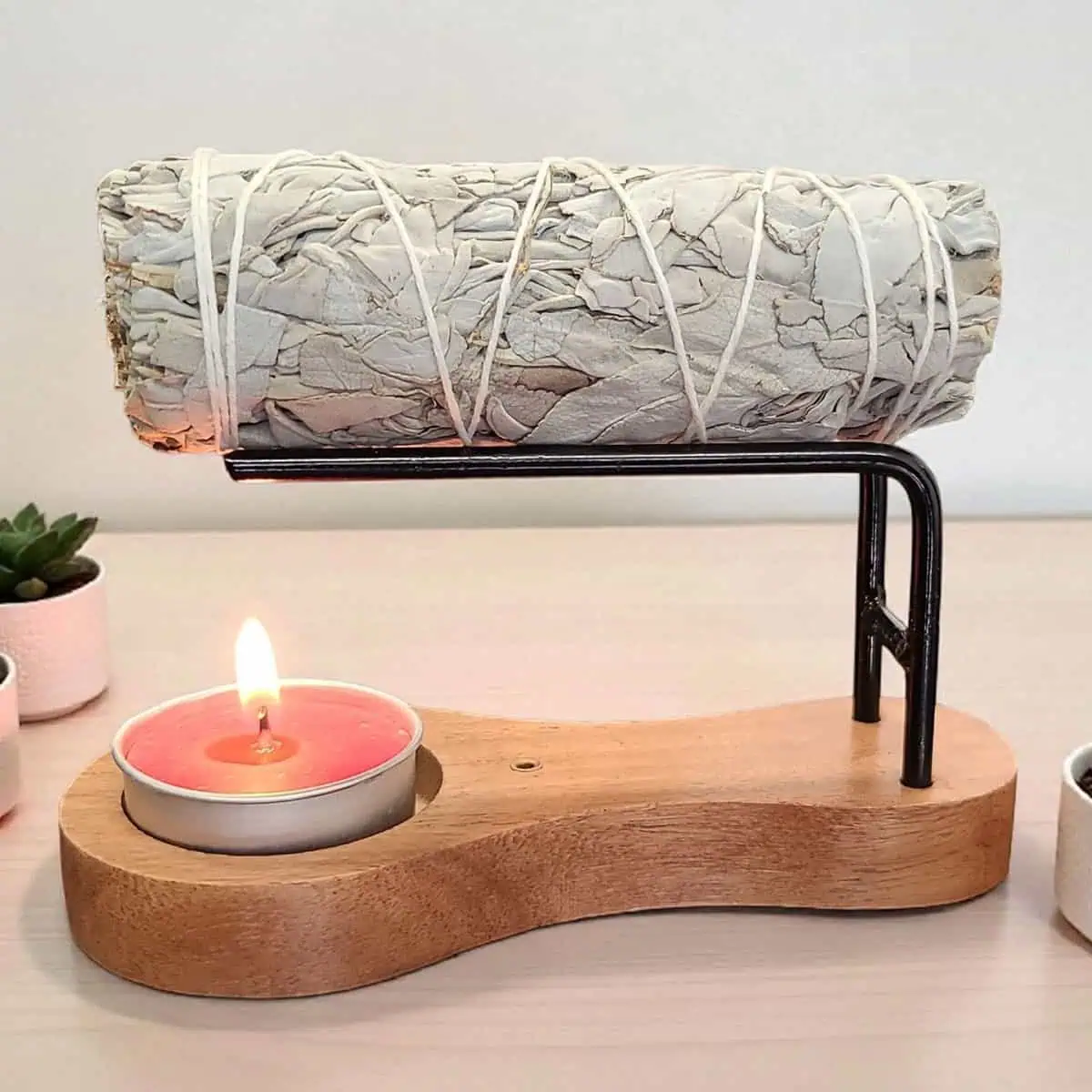 Modern wooden stand with sage bundle, candle, and small potted plants for spiritual practices.
