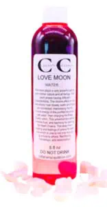 Bottle of Love Moon water with pink rose petals around it, on a white background.