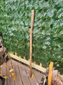 A natural wooden staff with a slightly curved shape, standing upright against a leafy background.