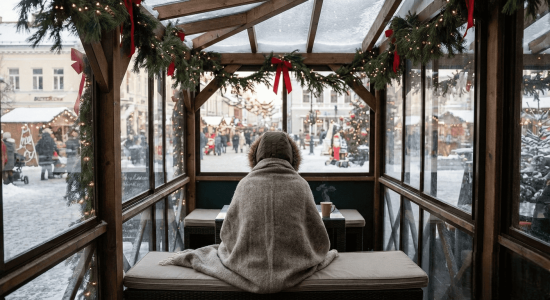 A person wrapped in a cozy blanket sits alone, gazing out at the holiday holiday lights and bustling crowd.